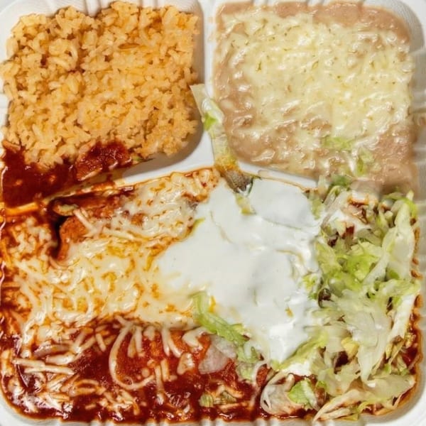A Mexican combination plate with rice, refried beans, enchiladas, sour cream, and lettuce.