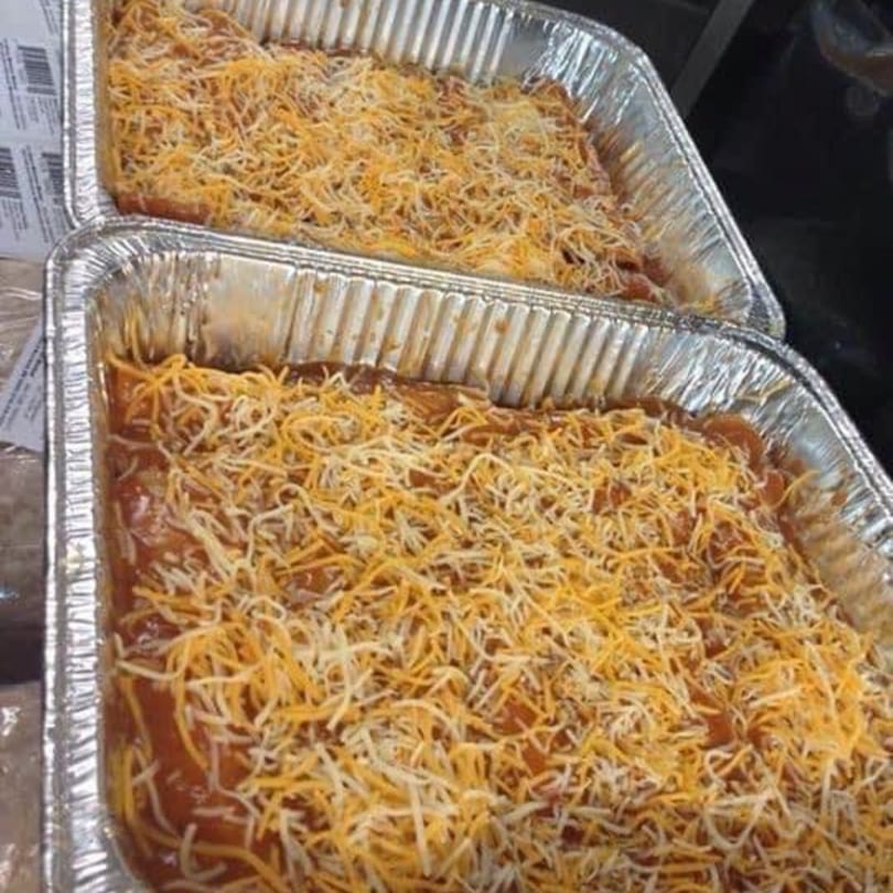 Two foil pans filled with a red sauce dish topped generously with shredded cheese.