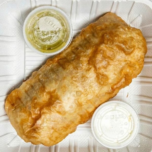 Golden-fried burrito with two small sauce containers, one green and one white, in a takeout tray.